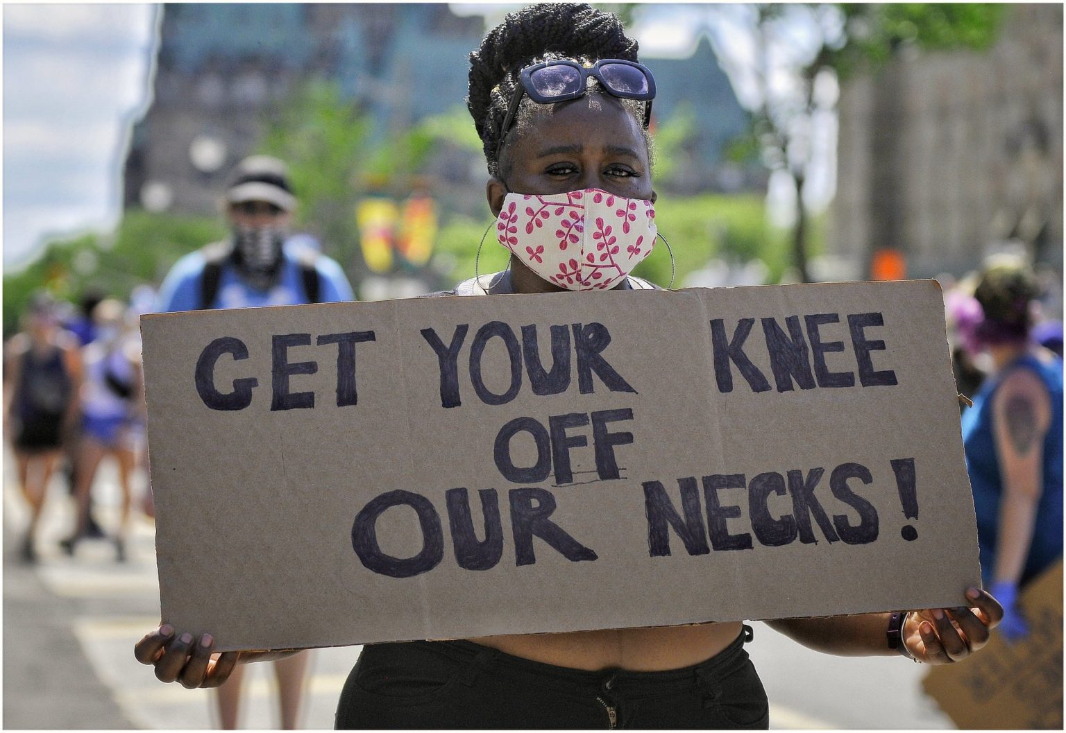 A protestor holding a sign that reads, "Get Your Knee Off Our Necks!"